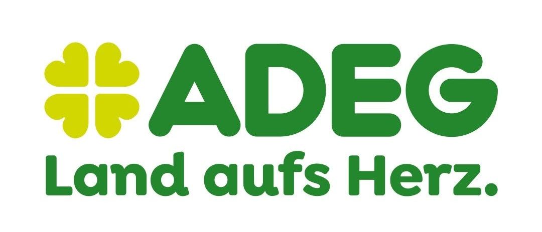 Das ADEG-Logo zeigt ein grünes Kleeblatt mit dem Text 'ADEG Land aufs Herz' in grüner Schrift. Das Kleeblatt ist gelb mit grünen Blättern.