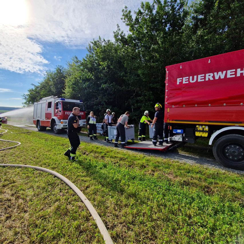 Feuerwehrleute sind draußen mit einem Feuerwehrauto, einem roten Lastwagen und einer Feuerwehrschläuche, an einem sonnigen Tag.