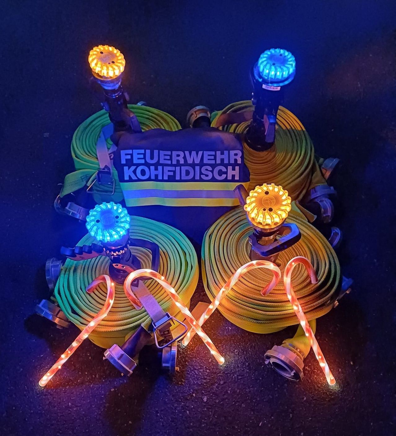 Die Ausrüstung eines Feuerwehrmanns mit beleuchteten Schläuchen und Düsen auf dunklem Hintergrund. Die Ausrüstung umfasst gelbe und blaue Lichter und ein Etikett mit der Aufschrift 'Feuerwehr Kohfisch.'