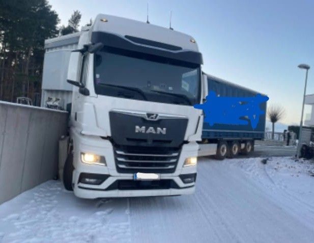 Ein weißer MAN-Lkw mit eingeschalteten Scheinwerfern ist im Schnee stecken geblieben und hat eine Betonbarriere getroffen.