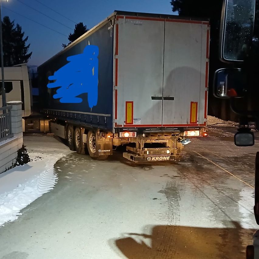 Ein blauer und weißer Anhänger-Lkw ist auf einer nassen Straße geparkt, wobei das Heck sichtbar ist und ein blauer Marker an der Seite angebracht ist.