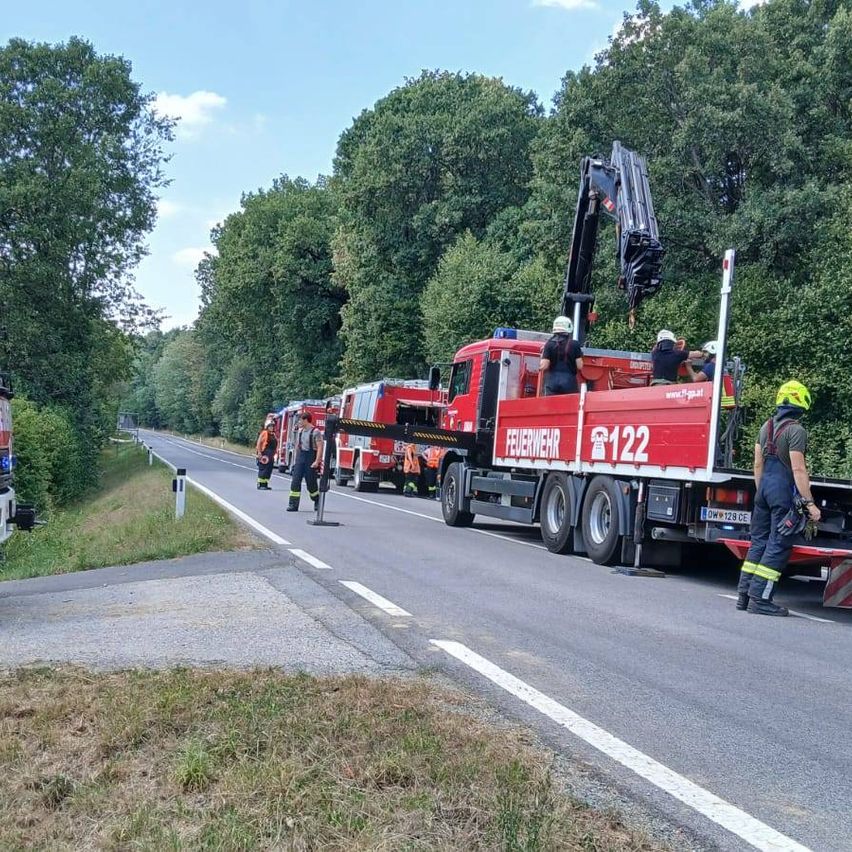Feuerwehrleute benutzen einen Kran, um einen LKW von der Straße zu entfernen, mit mehreren Feuerwehrwagen in der Nähe.