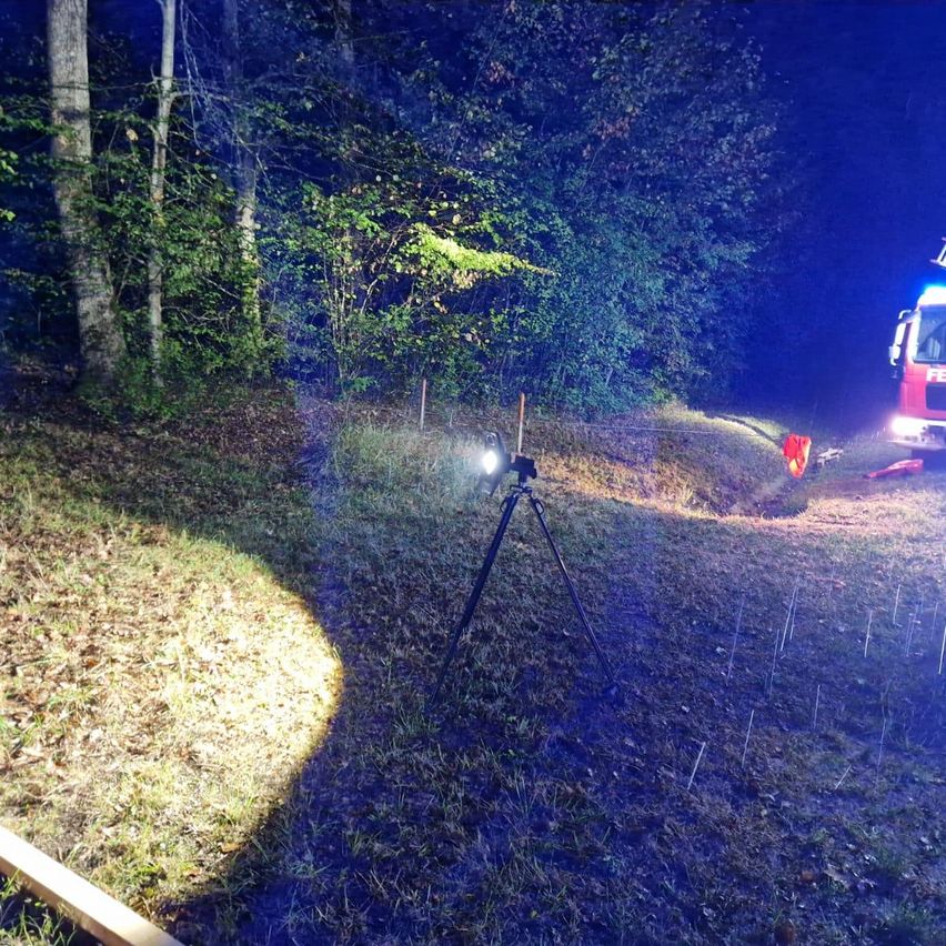 Ein Feuerwehrauto steht nachts auf einer unbefestigten Straße im Wald. Ein Stativ mit einer Kamera ist in der Nähe aufgestellt.