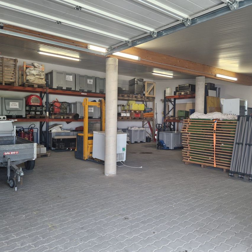 A warehouse with shelving units, metal storage boxes, a forklift, and various tools. The ceiling has fluorescent lights and the floor is paved with tiles.