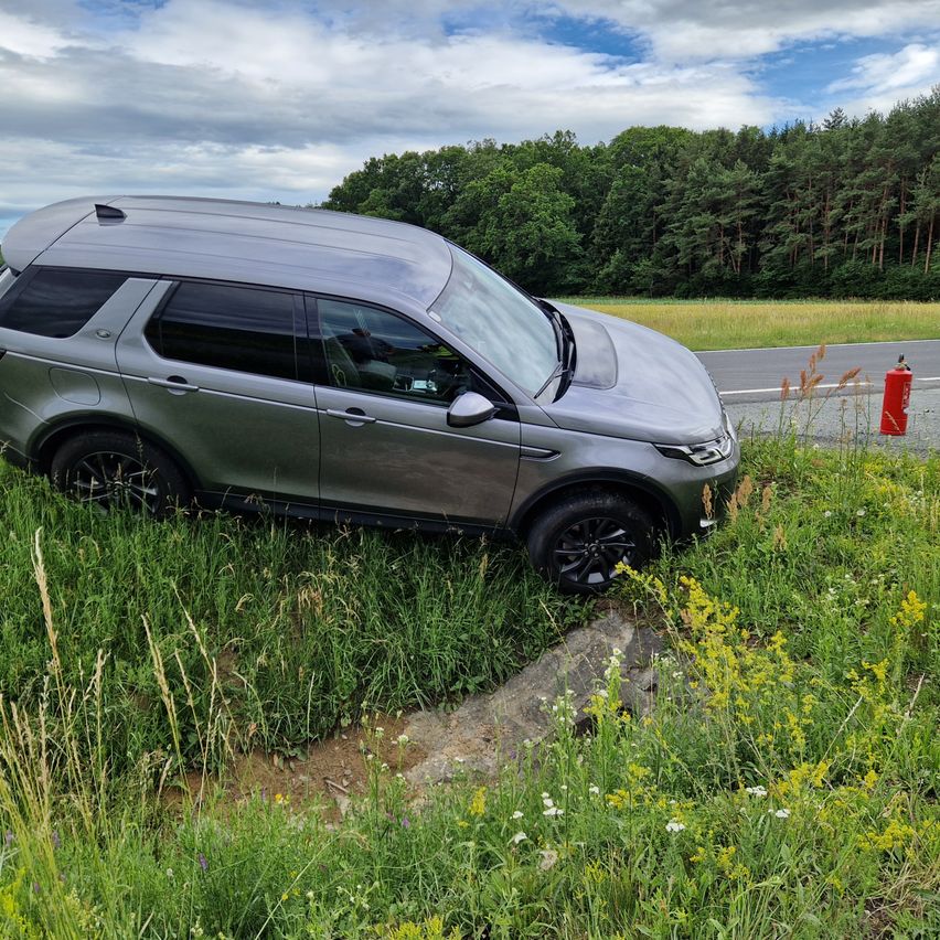 A gray SUV is parked on the side of the road, with its front wheel on the grass, next to a red fire extinguisher.