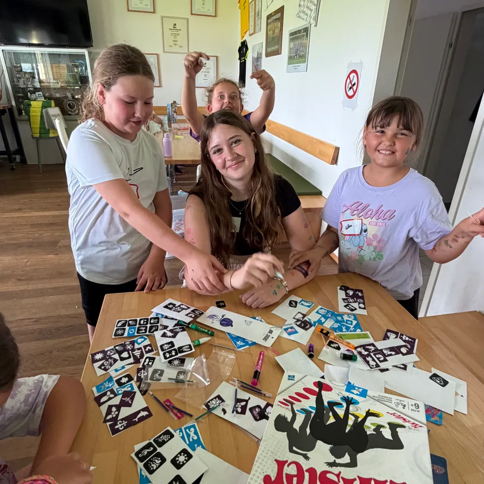 Eine Gruppe junger Mädchen sitzt um einen Tisch mit temporären Tattoos, lächelt und posiert für ein Foto.