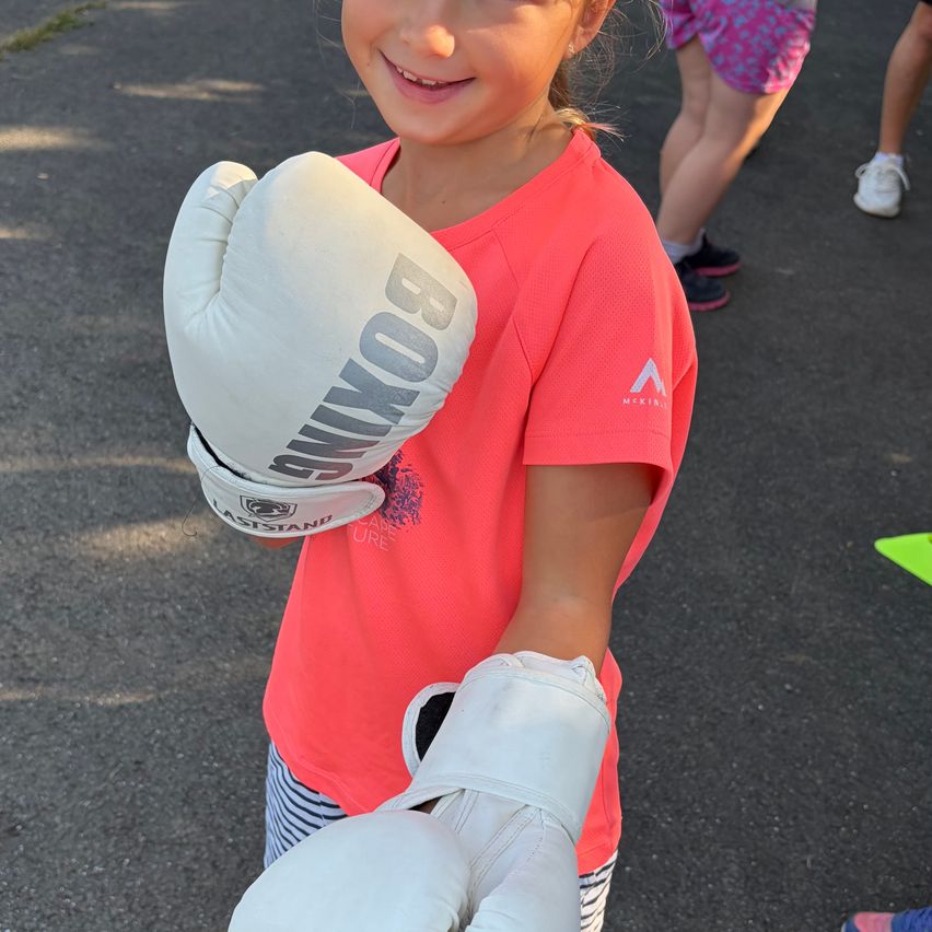 A young girl wearing a red shirt and boxing gloves is smiling and posing for a photo.
