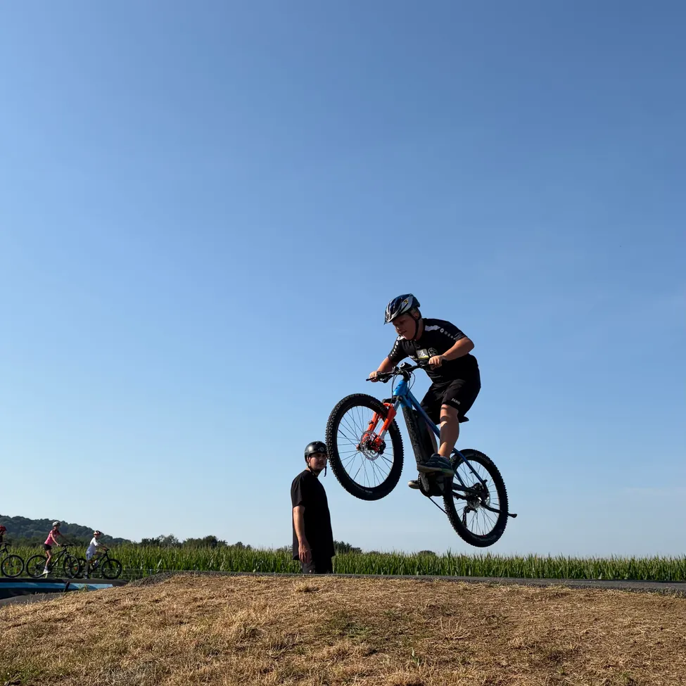 Eine Person führt einen Fahrradsprung auf einer Erdrampe unter einem klaren blauen Himmel durch.