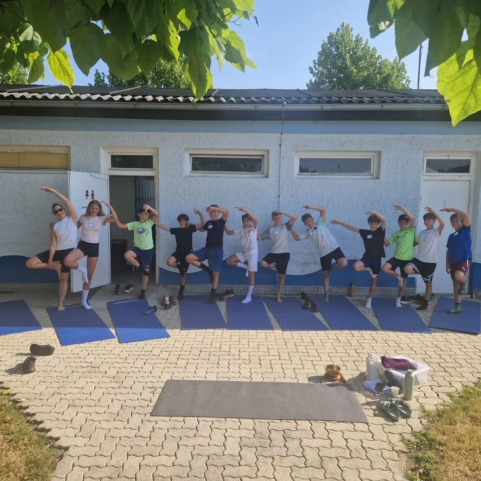 Eine Gruppe junger Menschen macht Yoga-Posen vor einem Gebäude mit einem Ziegelboden.