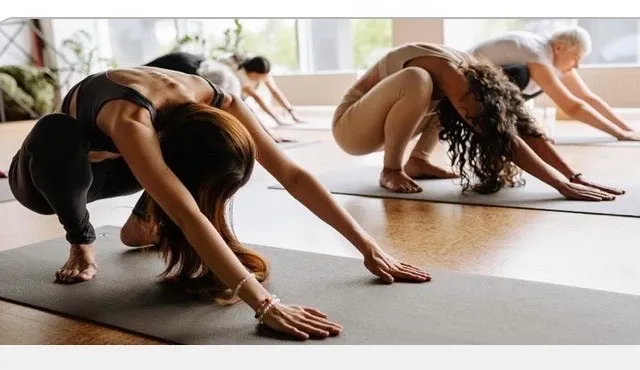 Mehrere Frauen praktizieren Yoga in einem Studio, wobei eine Frau im Vordergrund einen Kopfstand macht.
