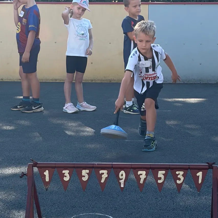 Vier Jungen stehen auf einem Spielplatz mit Zahlen auf einer Hürde vor ihnen. Der Junge vorne ist dabei, einen Ball zu werfen.