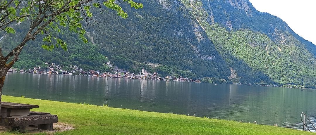 Ein ruhiger Seeblick mit üppigem Grün und Bergen im Hintergrund. Ein kleines Dorf mit Gebäuden und einer Kirche liegt am Ufer.