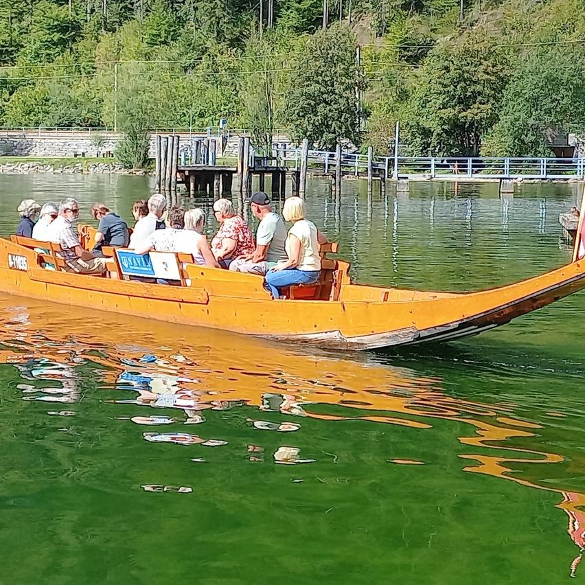Eine Gruppe von Menschen fährt mit einem gelben Boot auf einem Fluss, mit einem Steg und Bäumen im Hintergrund.