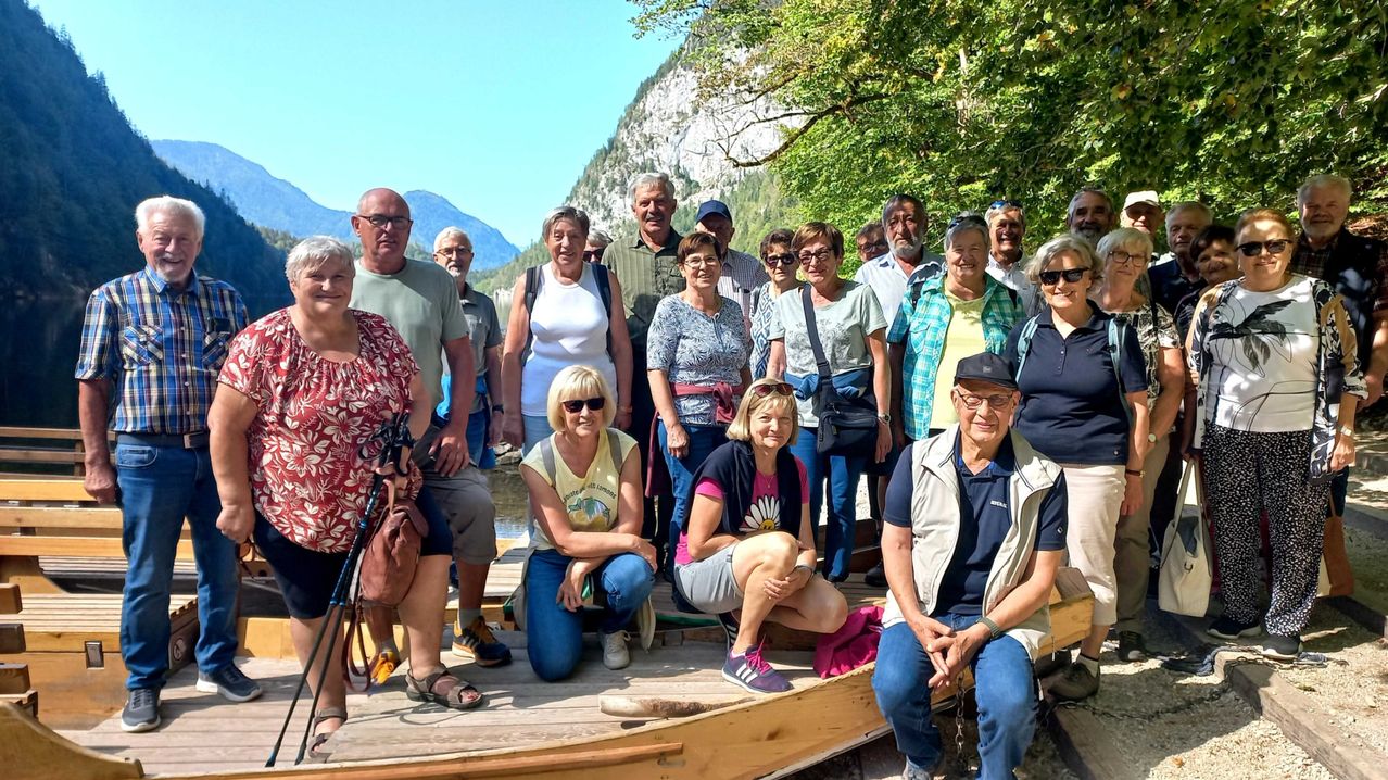 Eine Gruppe von Menschen, einige sitzend und einige stehend, posiert für ein Foto auf einer Holzplattform in der Nähe eines Flusses, mit Bergen und Bäumen im Hintergrund.