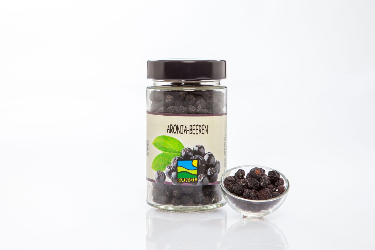 A jar labeled 'Aronia-Beeren' with dried black berries inside. Next to it is a small bowl with more berries.