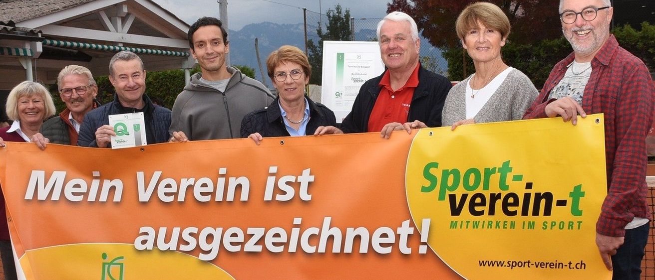 Eine Gruppe Erwachsener steht auf einem Tennisplatz und hält ein Banner mit der Aufschrift 'Mein Verein ist ausgezeichnet!' mit einem Logo und einer Website.