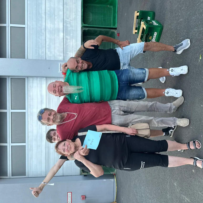 Vier Personen posieren für ein Foto vor einem Gebäude mit Lagerboxen und Kisten im Hintergrund. Sie lächeln und scheinen Freunde zu sein.