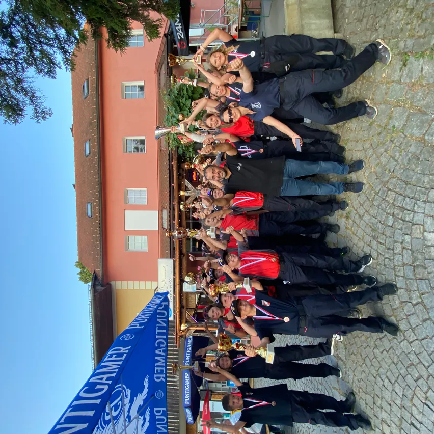 Eine Gruppe von Menschen in Uniformen, die Trophäen halten und vor einem Gebäude für ein Foto posieren.