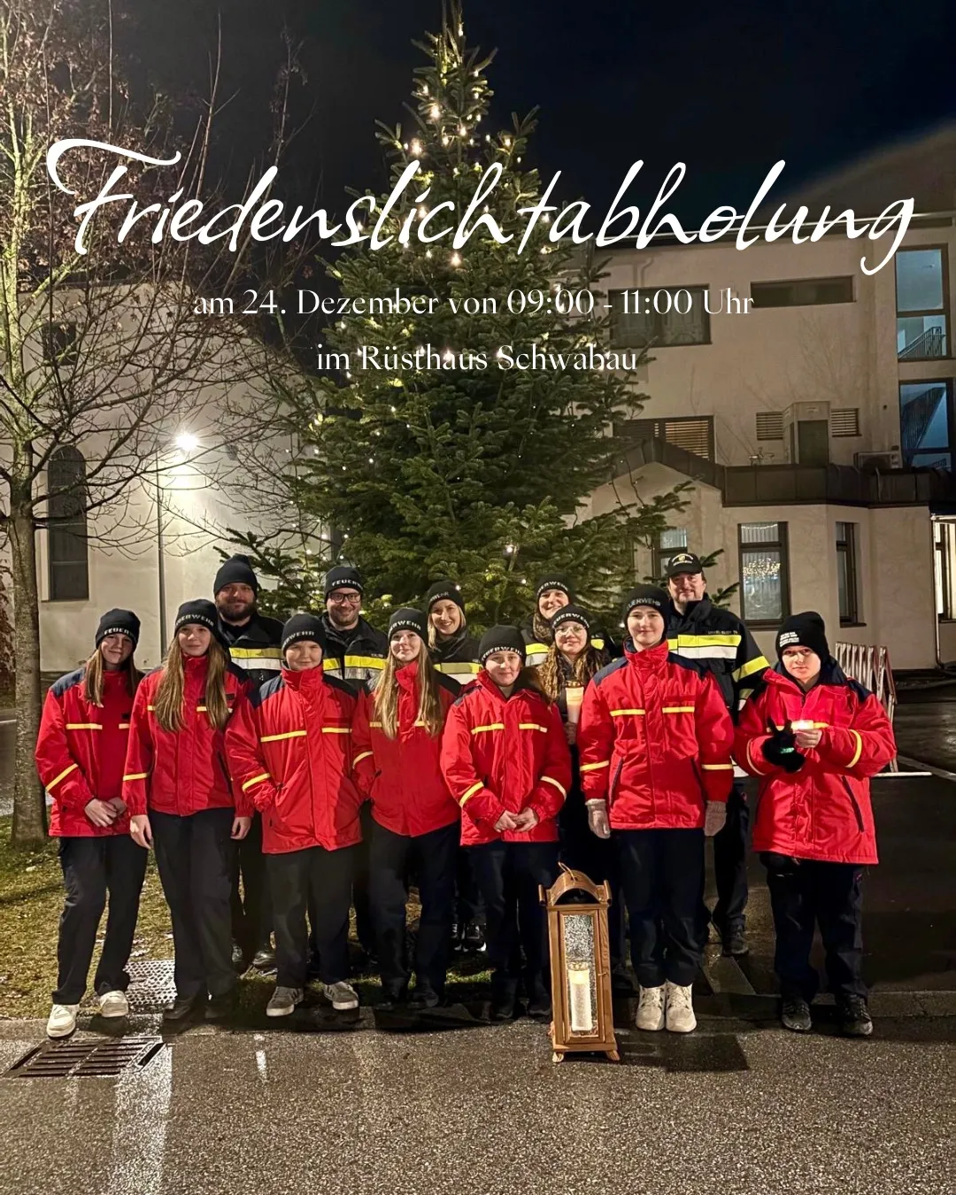 Eine Gruppe von Menschen in roten Uniformen steht vor einem Weihnachtsbaum, mit einer brennenden Kerze in einem Laternen. Hinter ihnen ist ein Gebäude mit vielen Fenstern.