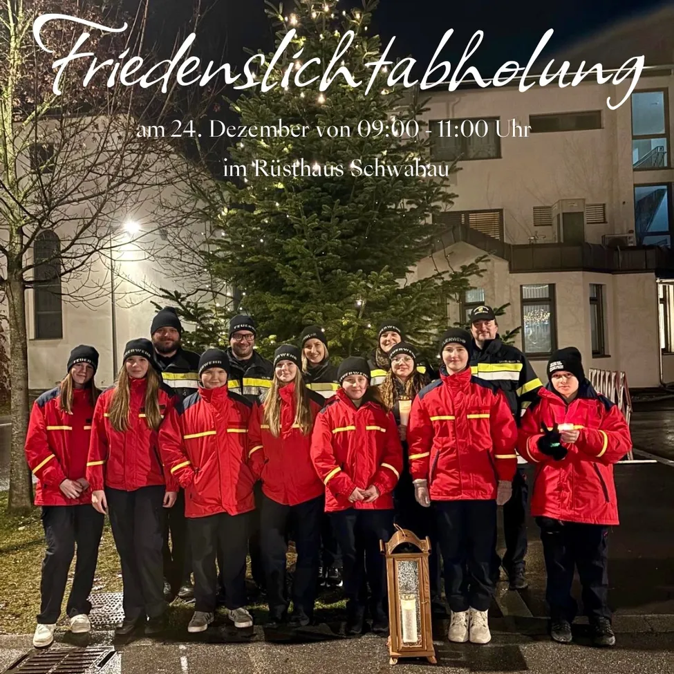 Eine Gruppe von Menschen in roten Uniformen steht vor einem Weihnachtsbaum, mit einer brennenden Kerze in einem Laternen. Hinter ihnen ist ein Gebäude mit vielen Fenstern.