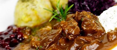 Ein weißer Teller hat ein Fleischgericht mit Soße, ein Stück Brot und etwas Rotkohl.