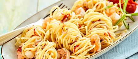Ein Teller mit Pasta, Garnelen, roten Chiliflocken und Zwiebeln auf einem blauen Tuch mit einer Gabel.