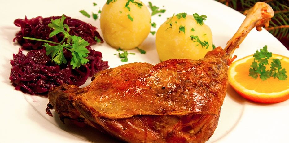 Ein Teller mit gebratener Ente, Rotkohl und Kartoffelpüree, garniert mit Petersilie, begleitet von einer Orangenscheibe.