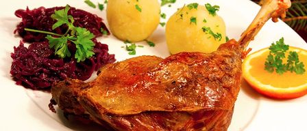 Ein Teller mit gebratener Ente, Rotkohl und Kartoffelpüree, garniert mit Petersilie, begleitet von einer Orangenscheibe.