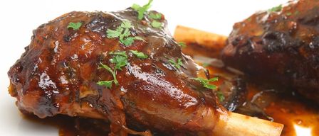 Eine Nahaufnahme eines gebratenen Lammkeulenstücks mit Soße, garniert mit frischen Kräutern, auf einem weißen Teller.