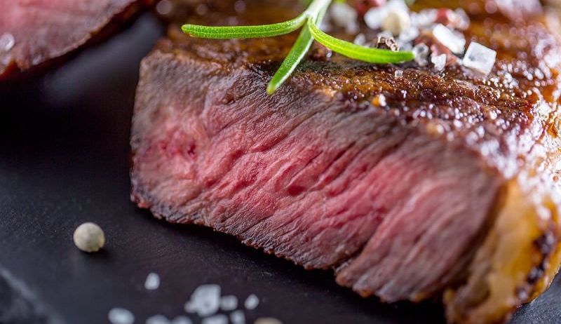 Ein Nahaufnahme eines gekochten Steaks mit Rosmarin und Gewürzen. Das Steak hat eine reiche, rötlich-braune Farbe und eine leicht knusprige Textur.