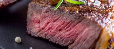 Ein Nahaufnahme eines gekochten Steaks mit Rosmarin und Gewürzen. Das Steak hat eine reiche, rötlich-braune Farbe und eine leicht knusprige Textur.