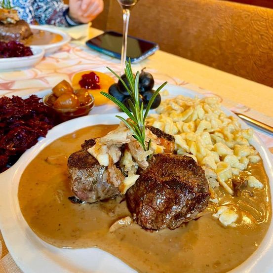 Ein Teller mit Steak in cremiger Sauce, garniert mit einem Rosmarinzweig, begleitet von Kartoffelpüree und Rotkohl.