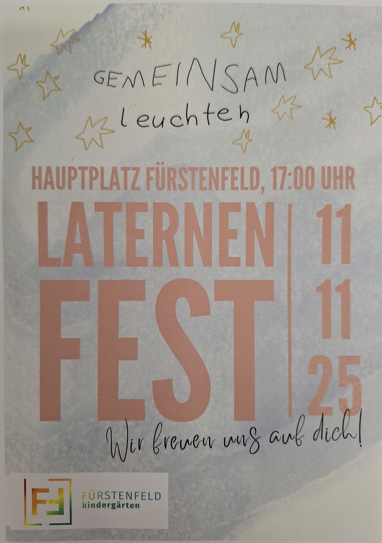 Ein Plakat bewirbt das Laternenumzug-Fest am Hauptplatz von Fürstenfeld um 17:00 Uhr. Das Plakat zeigt eine Reihe von Sternen und einen Slogan, der lautet: 'Wir freuen uns auf dich!' Das Datum des Festivals ist der 25. November.