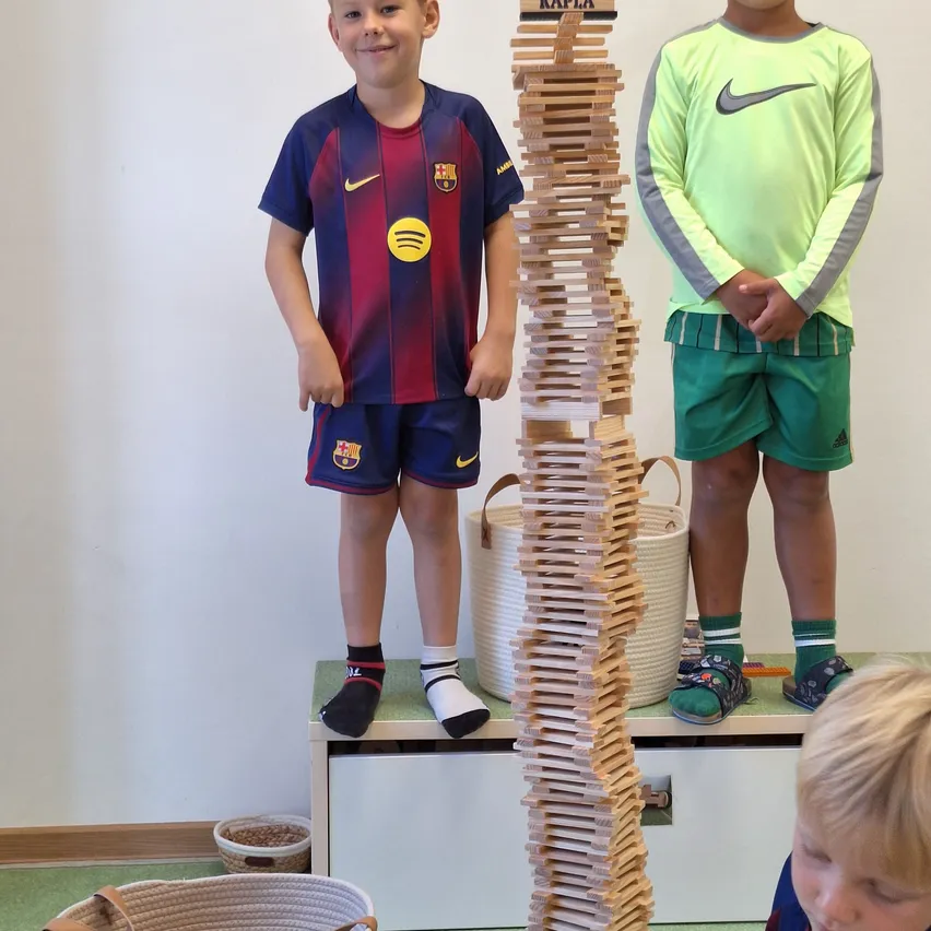 Zwei Jungen stehen neben einem hohen Stapel Holzklötzen, einer trägt ein Barcelona-Fußballtrikot und der andere ein grünes Nike-Shirt.