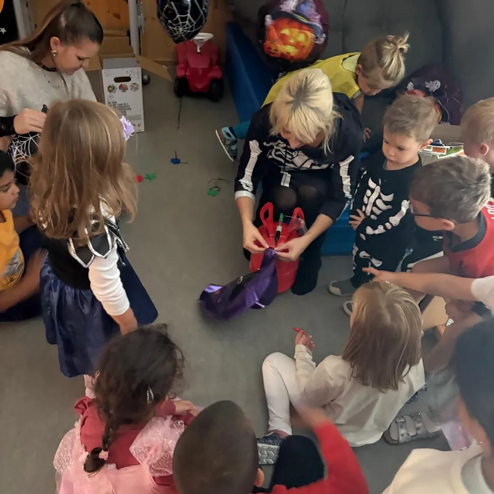 Eine Gruppe von Kindern in Kostümen versammelt sich um eine Frau, die Tüten mit Süßigkeiten verteilt.