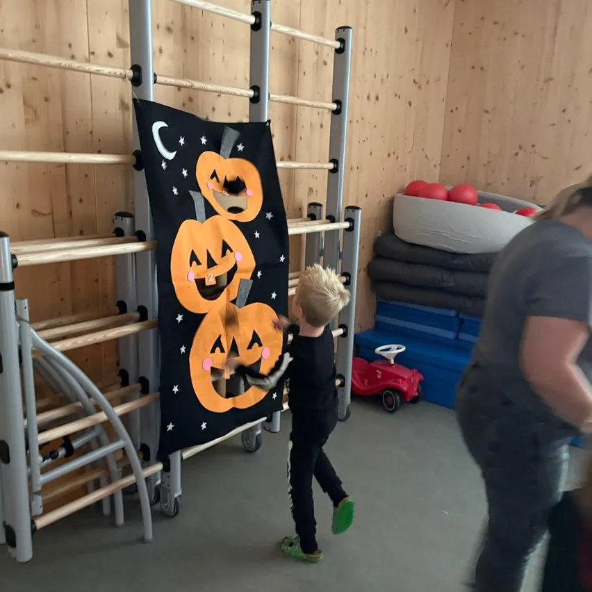 A young boy is playing with a Halloween-themed banner in a room with wooden walls and a red toy car.