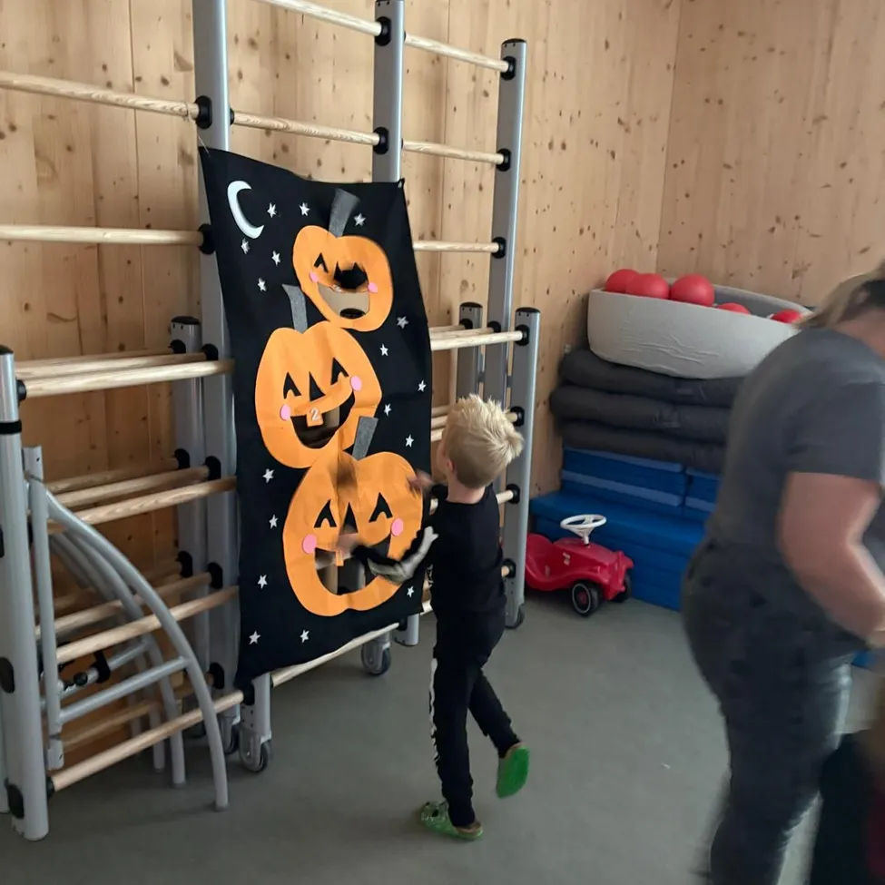 Ein kleiner Junge spielt mit einem Halloween-Banner in einem Raum mit Holzwänden und einem roten Spielzeugauto.