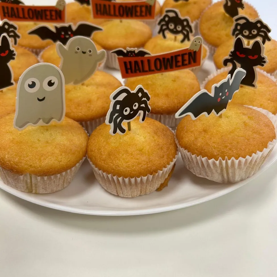 Eine Platte mit Halloween-Cupcakes, die mit verschiedenen Dekorationen wie Geistern, Fledermäusen und Spinnen verziert sind.
