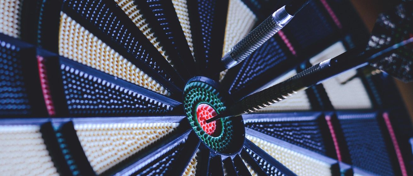 Eine Nahaufnahme eines Dartboards mit drei eingesteckten Darts. Das Dartboard hat einen bunten Bullseye.