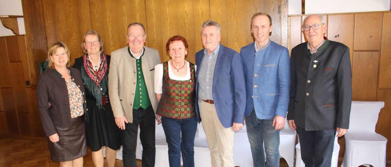 Eine Gruppe von Erwachsenen, sowohl Männer als auch Frauen, posiert für ein Foto in einem Raum mit Holzwänden. Sie lächeln und stehen eng beieinander.