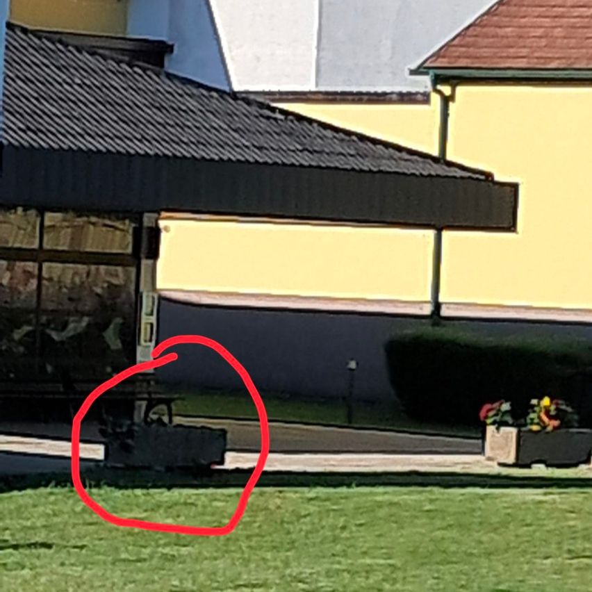Ein Außensitzbereich mit einem Vordach befindet sich in der Nähe eines Gebäudes. Ein Tisch und Stühle sind unter dem Vordach aufgestellt, und ein roter Kreis hebt einen bestimmten Bereich hervor.