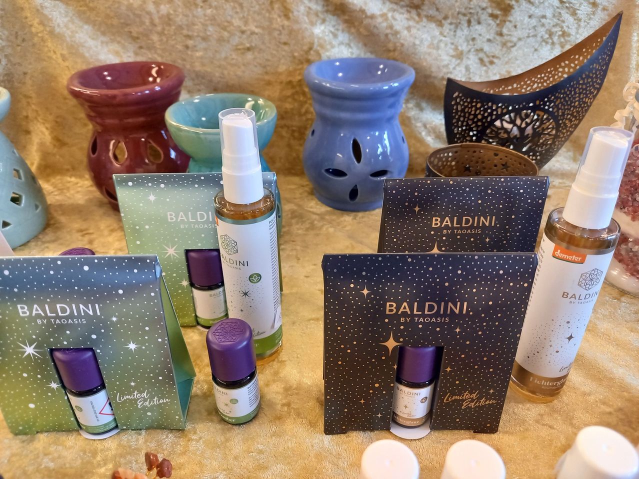 A collection of Baldini by Taoasis products including essential oils, diffusers, and candles, arranged on a beige surface.