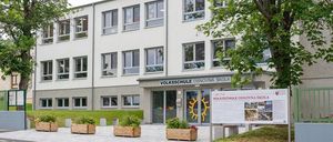 Die Vorderseite eines Erwachsenenbildungszentrums mit mehreren Fenstern und einem Schild, das 'Volksschule Osnovna Skole' lautet. Ein Plakat ist an einem Pfosten vor dem Eingang befestigt.