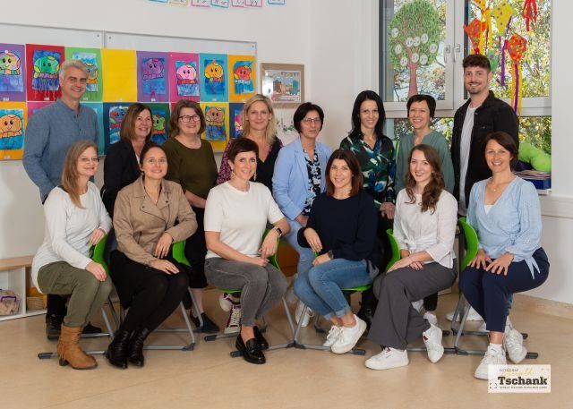 Eine Gruppe von Menschen, darunter sowohl Männer als auch Frauen, posiert für ein Foto in einem Raum mit farbenfrohen Gemälden an der Wand.