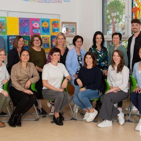 Eine Gruppe von Menschen, darunter sowohl Männer als auch Frauen, posiert für ein Foto in einem Raum mit farbenfrohen Gemälden an der Wand.