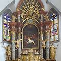 Ein kunstvoller Altar in einer Kirche mit Buntglasfenstern und Engelstatuen. In der Mitte befindet sich ein goldenes Gemälde einer Szene.