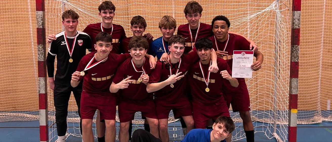 Eine Gruppe junger männlicher Athleten in roten Trikots, Medaillen und Turnschuhen posiert vor einem Tornetz für ein Foto.