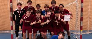 Eine Gruppe junger männlicher Athleten in roten Trikots, Medaillen und Turnschuhen posiert vor einem Tornetz für ein Foto.