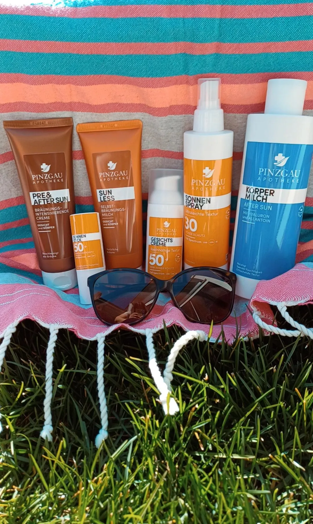 Eine Sammlung von Sonnenschutzprodukten von Pinzgau Apotheke liegt auf einer Decke über Gras.
