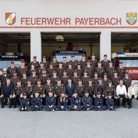 Ein Gruppenfoto der Feuerwehrleute aus Payerbach vor ihrem Feuerwehrhaus mit Feuerwehrautos im Hintergrund.